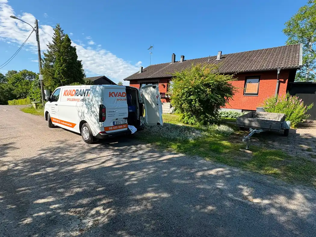 Kvadrants spolbil utanför ett rött hus på landet vid avloppsspolning av ett fritidshus med dålig lukt