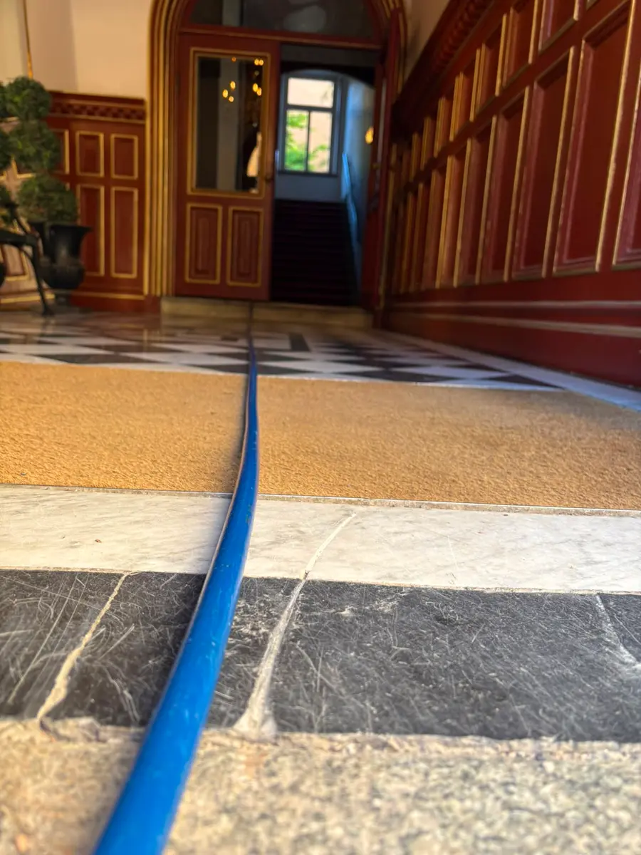 Spolslang draget genom porten över marmorgolvet vid stamspolning i en sekelskiftes-BRF på Östermalm