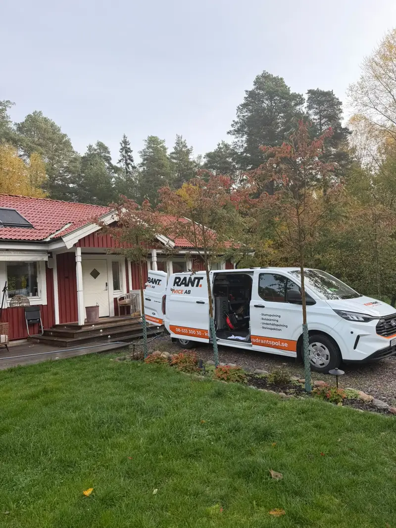 Kvadrants spolbil med öppen sidodörr på uppfarten till en röd villa i Täby vid underhållsspolning
